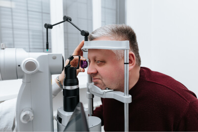 Перевірка зору в Binocular чоловіку з чорно-сивим волоссям в темно-червоній кофті